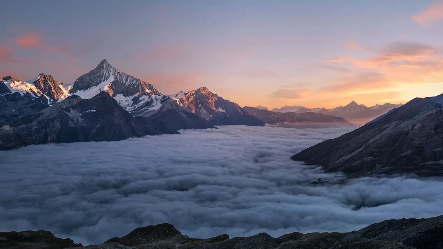 Mountain peaks rising above a layer of cloud at first light.